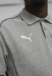 Grijze polo shirt met een kraag, voorzien van een wit Puma-logo op de borst en contrasterende donkere stiksels langs de schouders.