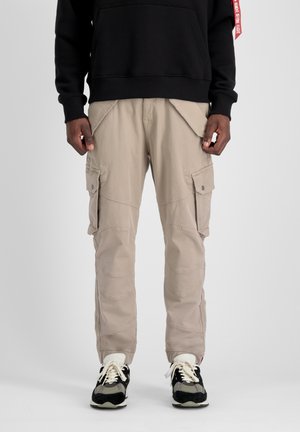 Beige Cargo-Hosen mit mehreren Seitentaschen, verstärkten Knie-Nähten und lockerer Passform, kombiniert mit schwarzen und grauen Turnschuhen.