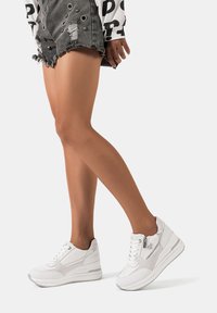 Sneakers sportivi bianchi con una finitura testurizzata, dotati di chiusura con zip, suola ammortizzata e vari pannelli di materiali per un contrasto di design.