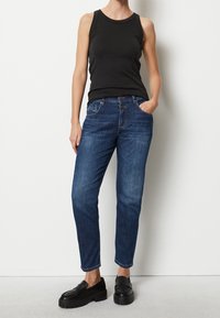 Top senza maniche nero abbinato a jeans in denim blu. I jeans presentano una vestibilità comoda, design a cinque tasche e un lavaggio chiaro con leggere sfumature di sbiadimento.