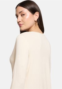 Cremiges Langarmshirt mit rundem Ausschnitt. Weicher, leichter Stoff mit lockerer Passform. Verfügt über minimale Nähte und eine glatte Textur.