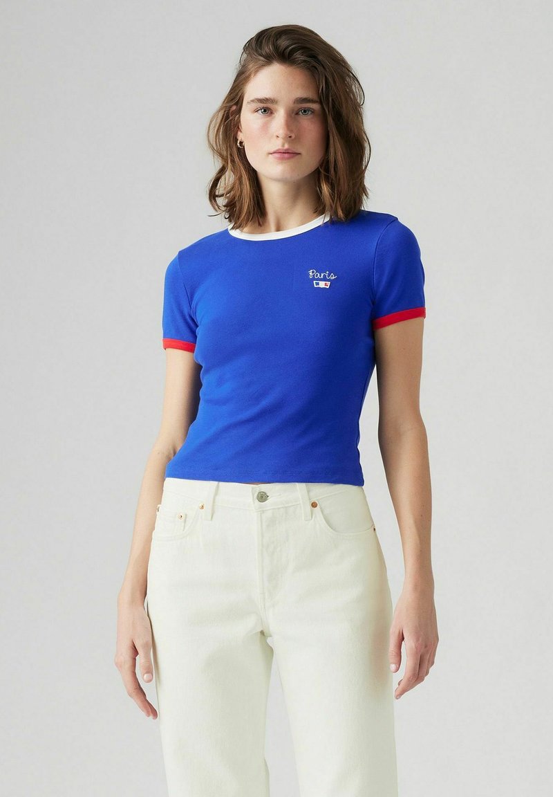 Blue cotton t-shirt with white collar and red sleeves, featuring a small embroidered "Paris" logo on the chest, paired with white pants.