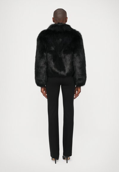 Chaqueta de pelaje sintético negro con un cuello alto, mangas largas y un acabado texturizado, combinada con pantalones negros ajustados y tacones.