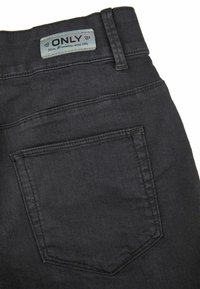 Jean de mezclilla negro con un bolsillo trasero, etiqueta azul con "ONLY" y costuras visibles. Textura suave, diseño de talle medio.