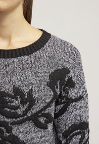 Czarny i szary sweter z teksturowanym wzorem dzianiny oraz kwiatowymi wzorami, okrągłym dekoltem i prążkowanym kołnierzem.
