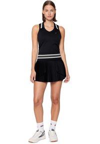 Abito sportivo nero con top a canotta a coste dotato di dettagli sulle spalle, gonna plissettata e cintura a righe. Indossato con sneakers bianche.