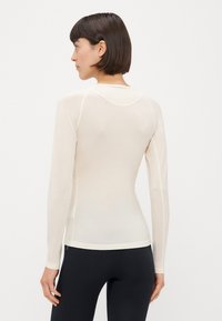 Haut à manches longues de couleur crème claire, au design ajusté, fabriqué en tissu doux et extensible. Équipé d'un col rond et de coutures contrastées le long des coutures.