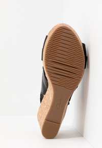 Sandale compensée avec semelle en liège, tige en cuir noir et semelle extérieure en caoutchouc texturé affichant le logo "Clarks".