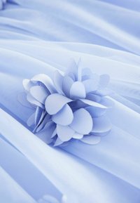 Blødt lyseblåt stofblomst med lagdelte kronblade, der hviler på en glat, matchende lyseblå stofbaggrund med bløde folder.