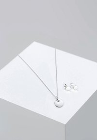 Collana in argento con un pendente circolare, caratterizzata da una catena elegante. Accompagnata da orecchini a bottone rotondi abbinati, entrambi con una finitura lucida.