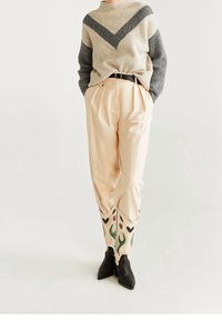 Pull en tricot à rayures grises et beiges ; pantalon plissé beige ; bottes de cowgirl crème ornées de motifs floraux rouges et verts.