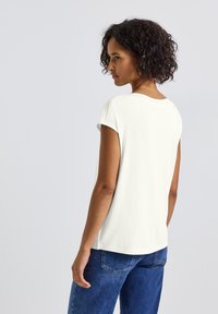 Vit t-shirt med kort ärm och rund halsringning, mjuk textur och avslappnad passform; kombinerad med blå denimjeans med lätt blekning och fickor.