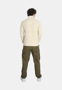 Pullover in crema spesso con colletto alto, texture a costine, abbinato a pantaloni cargo verdi oliva larghi con multiple tasche e una vestibilità rilassata.