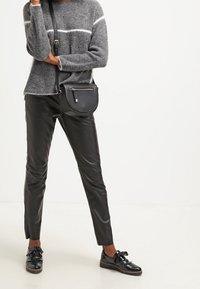 Pull gris duveteux avec des rayures blanches, pantalon en cuir noir, et chaussures en cuir verni noir avec des nœuds. Le sac possède une fermeture éclair.