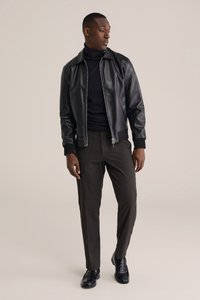 Svart skinn-bomberjacka, marinblå polotröja, grå byxor och svarta skor. Slät textur, figursydd design och minimalistiska detaljer.