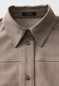 Bruin geruit overhemd met een button-down kraag, voorzien van een subtiele textuur en een logo label op de nek. Twee voorzakken zijn zichtbaar.