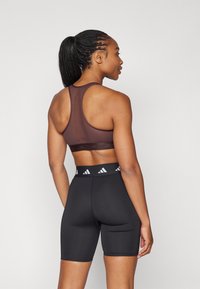 Brun sports BH med racerback-design, kombinert med høyt midje svarte shorts med en hvit logo elastikk. Glatt stofftekstur.