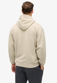 Sudadera con capucha beige, con puños y dobladillo de canalé, que presenta una textura suave y un corte relajado. Diseñada para la comodidad y el uso casual.