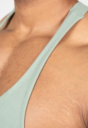 Lichtgroene tanktop met een diepe V-halsontwerp, de stof lijkt zacht en rekbaar, waardoor de halslijn en de huidtextuur prominent zichtbaar zijn.