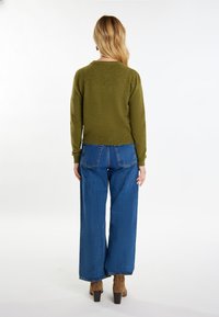 Maglione verde oliva con scollo tondo e orlo a costine, abbinato a jeans blu a gamba larga. Stivali beige alla caviglia completano l'outfit.