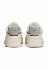 Sneakers in pelle beige con un tallone in suede grigio, dettagli rossi e logo "TOMMY HILFIGER" in rilievo sulla suola. Design con punta rotonda.