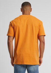 Oransje bomull t-skjorte med rund hals og korte ermer, med en avslappet passform og myk tekstur, sett fra baksiden.