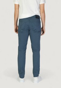 Pantalones ajustados azules hechos de una tela suave con bolsillos traseros; llevados con una camiseta blanca y zapatillas blancas; textura suave.