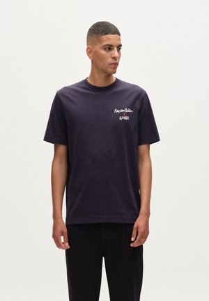 Navy katoenen T-shirt met een ronde halslijn en korte mouwen, met witte geborduurde tekst op de linkerkant van de borst. Eenvoudige, ontspannen pasvorm.