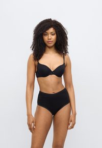 Μαύρο σουτιέν και σλιπ με ψηλή μέση. Το σουτιέν έχει λείες επιφάνειες και ένα μικρό φιόγκο στο κέντρο. Το σλιπ διαθέτει δαντελένιο τελείωμα στις άκρες.