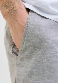 Gray linen pants with a textured finish, featuring a side pocket and detailed stitching along the edges. Close-up view of the fabric.