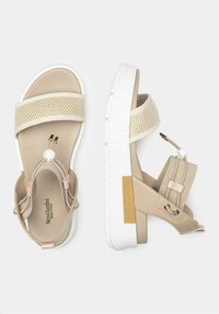 Beige sandals featuring mesh straps, a thick white sole, adjustable fastening, and a branded accent on the side. Suitable for casual wear.