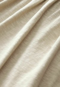 Beiger Stoff mit einer weichen, glatten Textur, der subtile Tonvariationen und ein schwaches, gewebtes Muster zeigt.