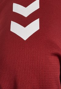 T-shirt de sport rouge avec une texture structurée, ornée de motifs en chevrons blancs bien en vue sur la poitrine.