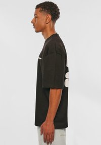 Tricou din bumbac negru cu mâneci scurte, croială relaxată, având un grafic alb pe spate. Textură fină cu decolteu rotund.