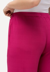 Pantaloni rosa a coste con una cintura liscia e tasche laterali, che presentano un design aderente. La texture è leggermente lavorata, sottolineando il comfort.