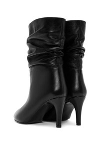 Bottines en cuir noir avec un design décontracté, des talons hauts effilés, une texture lisse et des détails froncés au niveau de la tige supérieure.
