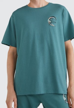 Osoba ubrana w turkusowy t-shirt z krótkim rękawem z małą grafiką fali i logo "O'Neill" po lewej stronie klatki piersiowej oraz dopasowane turkusowe szorty.