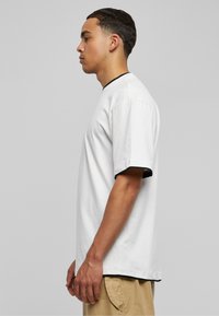 Vit bomulls t-shirt med korta ärmar, svart accenttrim på ärmslut och halsringning, avslappnad passform. Modell visas i profil.