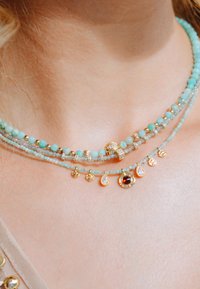Collier multi-couches avec des perles bleu clair, des accents dorés et des charms scintillants incluant des formes en goutte et rondes.