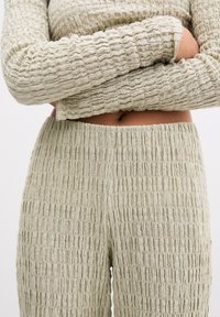 Beige gebreide top met textuur en bijpassende broek met een gekreukeld ontwerp. Beide kledingstukken hebben een rekbare pasvorm en geribbelde accenten.