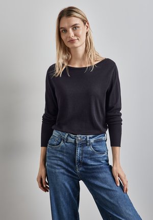 Maglietta nera a maniche lunghe in maglia con scollo ampio, abbinata a jeans blue a gamba larga. Entrambi i capi presentano una texture liscia e un design casual.
