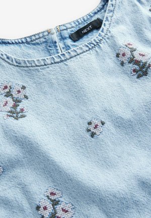 Hellblaue Jeansbluse mit Blumenstickerei in Weiß und Rot, runder Halsauschnitt und subtiler Textur. Markenlabel innen sichtbar.