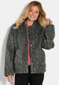 Grijze, fluffy textuur jack met grote knopen, opgerolde mouwen, twee voorkruiszakken en een ronde kraag, gelaagd over een roze top.