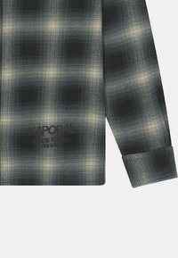 Camicia a maniche lunghe a quadri con tonalità verde scuro e nero, arricchita da linee bianche in contrasto. Include un logo nero stampato sul davanti.