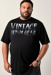 Camiseta de manga corta negra con texto grande en blanco y azul desgastado que dice "VINTAGE DENIM GEAR". Corte ligeramente holgado, confeccionada en material de algodón suave.