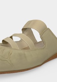 Chaussure plate beige avec des sangles élastiques et une semelle en caoutchouc, dotée de détails cousus et d'un logo Puma embossé sur le côté.