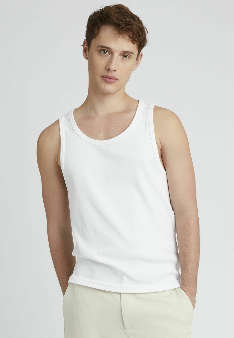 Débardeur blanc sans manches en coton lisse, avec un col rond classique et une coupe décontractée, associé à un short de couleur claire.