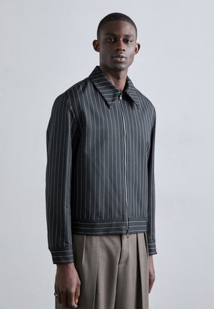 Schwarz gestreifte Zip-Jacke mit großem Kragen und gerippten Bündchen, versehen mit kontrastierenden weißen Linien und einer glatten Stofftextur.