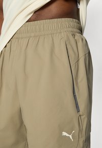 Μπεζ αθλητικά σορτς με ελαστική ζώνη μέσης, πλαϊνές τσέπες και αντίθετη σκουρόγκρι λεπτομέρεια. Διαθέτουν λευκό λογότυπο Puma στο κάτω μέρος του ποδιού.