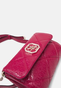 Rosa håndtaske i laklæder med quiltet mønster, guldfarvede beslag og et markant sekskantet logo på klaplukningen.